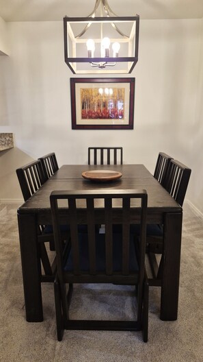 Ein Esszimmer mit einem rechteckigen Tisch, sechs Stühlen, einer Chandelierleuchtre und einem gerahmten Bild an der Wand.