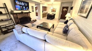 Ein Wohnzimmer mit einer Couch, einem Couchtisch, einem Fernseher, einem Kamin und einem Essbereich mit Stühlen und einem Tisch.