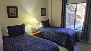 Ein Hotelzimmer mit zwei Betten, einem Nachttisch mit Lampe und einem Fenster mit Blick ins Freie.