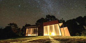 A modern house with large windows, a visible interior, and a starry night sky. - Proms Edge - Saltbush Villa (Yanakie)