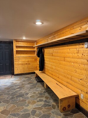 L’intérieur d’un chalet en bois, avec un banc, un porte-manteau et un sol carrelé en pierre.