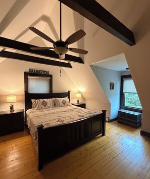 A bedroom with a sloped ceiling, a bed with patterned bedding, two bedside lamps, and a ceiling fan.