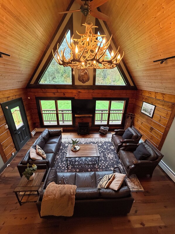 A cozy log cabin interior with a fireplace, leather sofas, a coffee table, and a chandelier.