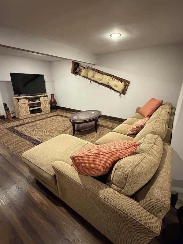 Una sala de estar con sofá, reposapiés y un televisor de pantalla plana sobre un mueble de madera.