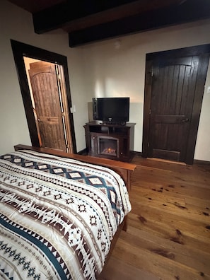 Un dormitorio con una cama, un televisor sobre un mueble bajo, una chimenea y dos puertas.