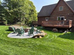 A wooden cabin with a deck, surrounded by a well-maintained lawn and large rocks.