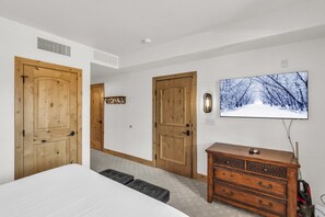 Une chambre à coucher avec un lit, une commode, deux portes et un téléviseur fixé au mur.