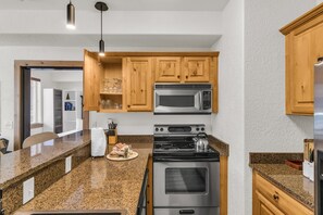 A kitchen with granite countertops, stainless steel appliances, wooden cabinets, and a hanging light fixture. - Silverado 310 | Canyons Village | Pool, Hot Tub & Walk to Ski (Park City)