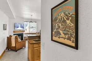 A living room with a fireplace, a television, and a kitchen area with a granite countertop. - Silverado 310 | Canyons Village | Pool, Hot Tub & Walk to Ski (Park City)