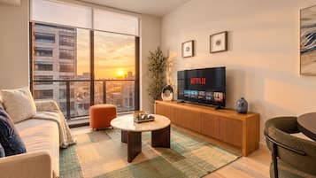 A modern living room with a large window, a flat-screen TV, a sofa, a coffee table, and a small side table.