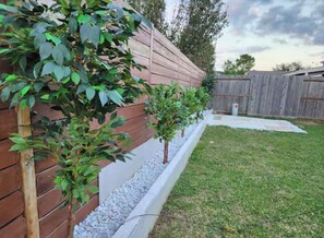 A wooden fence with a white trim, a small tree, and a grassy yard. - Luxurious 4BD/3.5 BTH home just minutes away from Houston! (Cypress)