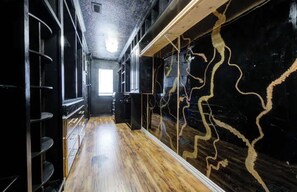 Un couloir doté d’un plancher en bois, de murs noirs ornés de motifs évoquant des veines dorées, et d’étagères métalliques.