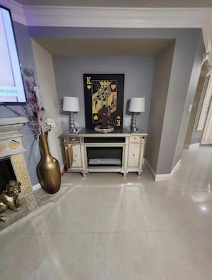 A room with a fireplace, a decorative vase, a framed artwork, and a console table with two lamps. - Luxurious 4BD/3.5 BTH home just minutes away from Houston! (Cypress)