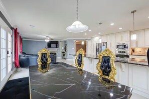 A modern kitchen with white cabinetry, a black marble island, and gold-framed chairs. - Luxurious 4BD/3.5 BTH home just minutes away from Houston! (Cypress)