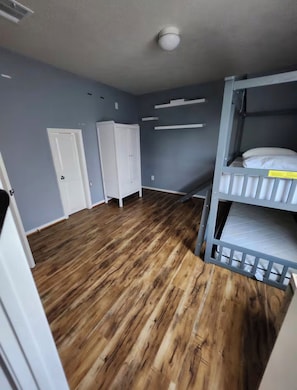 A room with a bunk bed, wooden flooring, a white door, and a white wardrobe. - Luxurious 4BD/3.5 BTH home just minutes away from Houston! (Cypress)