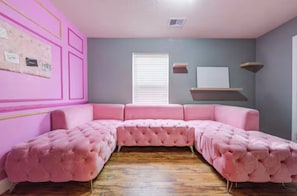 Un canapé d’angle rose dans une pièce dotée d’un plancher en bois et d’une fenêtre avec des stores.