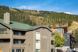 A hotel with a modern design, featuring a prominent 'The Edelweiss' sign, a green roof, and a view of a forested hillside. - New! Ski-In/Ski-Out Condo w/ Mountain Views, Fireplace & Balcony (Whitefish)