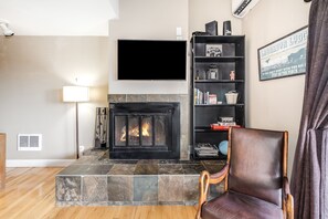 Ein Wohnzimmer mit Kamin, Flachbildfernseher, Bücherregal und Ledersessel.