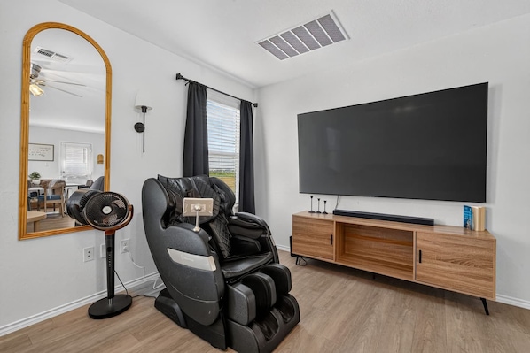 Un salon moderne doté d’un fauteuil massant, d’un téléviseur à écran plat et d’un meuble de rangement en bois.