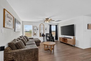 A modern living room with a sectional sofa, a ceiling fan, a flat-screen TV, and a dining table.