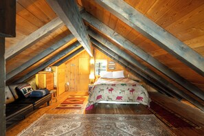 A cozy attic bedroom with a sloped ceiling, a bed with a patterned bedspread, a bench with cushions, and a rug. - New! Arrive by Boat | Lakefront Island Cabin on Echo Lake w/ Dock & Views (Bigfork)