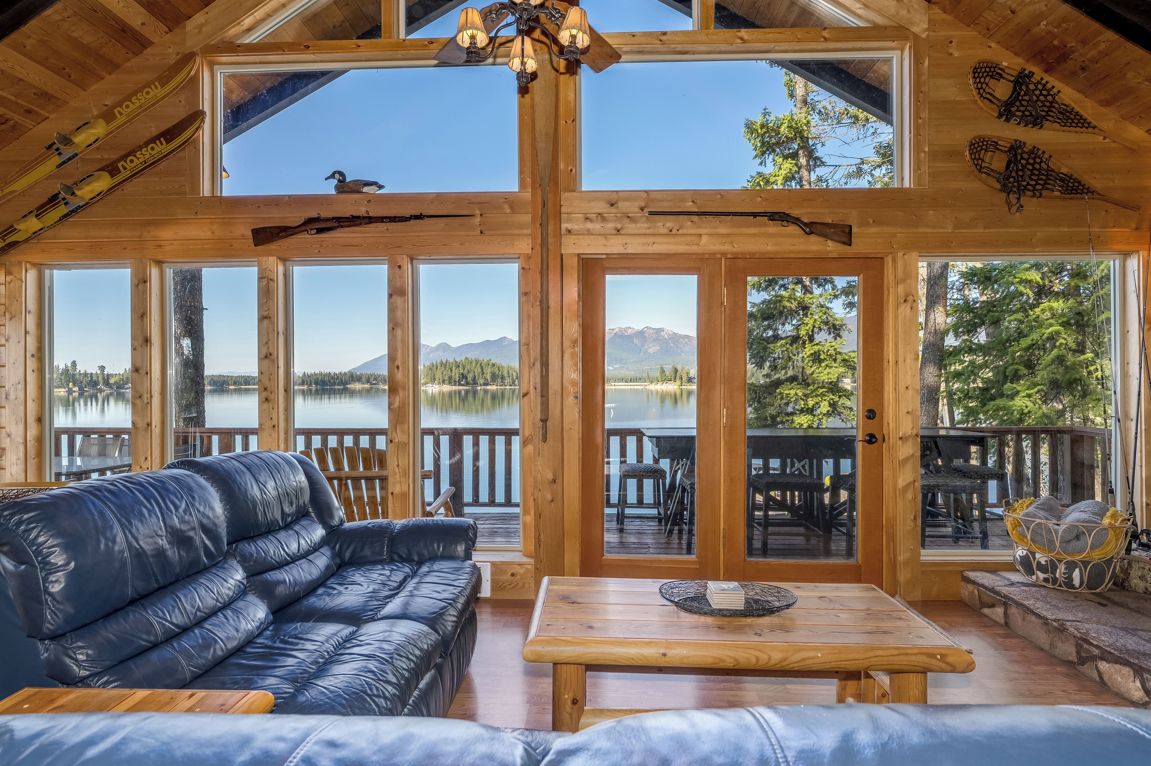 A cabin with a large wooden interior, a leather sofa, a dining table, and a view of a lake and mountains.
