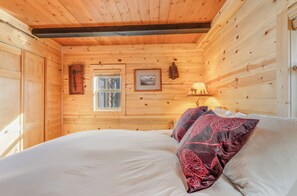 Une pièce de cabane en bois comprenant un lit, une fenêtre et une lampe fixée au mur.