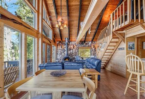 A cabin interior with a stone fireplace, wooden ceiling beams, and a dining area. - New! Arrive by Boat | Lakefront Island Cabin on Echo Lake w/ Dock & Views (Bigfork)