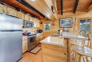 Cocina de cabaña de madera con refrigerador, microondas, estufa y gabinetes de madera.