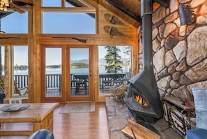 Une cabane dotée d’une cheminée en pierre, d’un intérieur en bois et offrant une vue sur un lac.