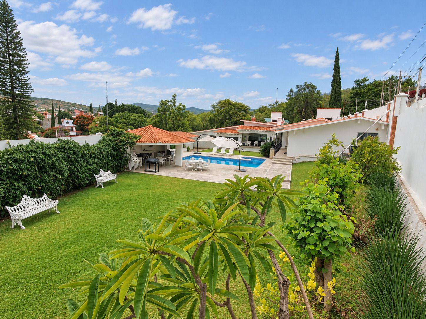 A residential backyard with a swimming pool, outdoor furniture, and a white fence.
