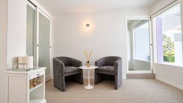 A modern room with two grey armchairs, a small round table, a glass cabinet with bottles, and a wall-mounted light fixture.
