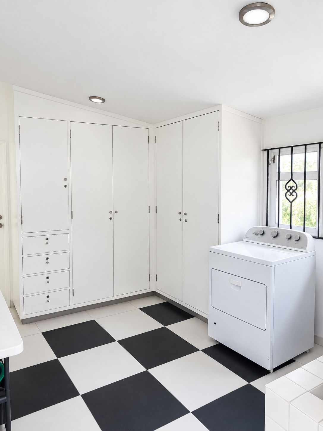 A laundry room with a white washing machine, a large white cabinet with drawers, and a black and white checkered floor.