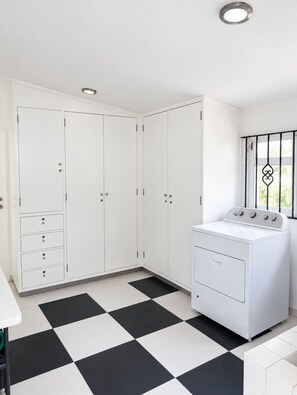 A laundry room with a white washing machine, a large white cabinet with drawers, and a black and white checkered floor. - Mansion Maria - 5 Luxury Suites & Heated Pool (San Felipe del Agua)