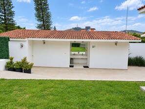 A modern building with a red-tiled roof, a covered outdoor area with a sink, and a grassy lawn.
