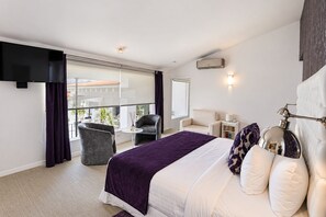 A modern hotel room with a large bed, a balcony with a view, a desk, and a chair.