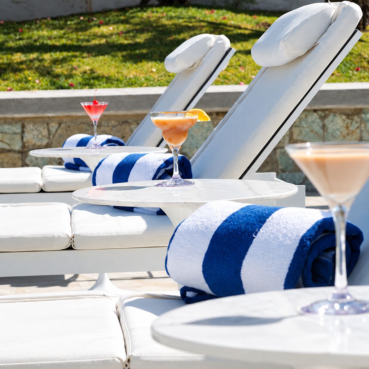 A row of sun loungers with towels and drinks.