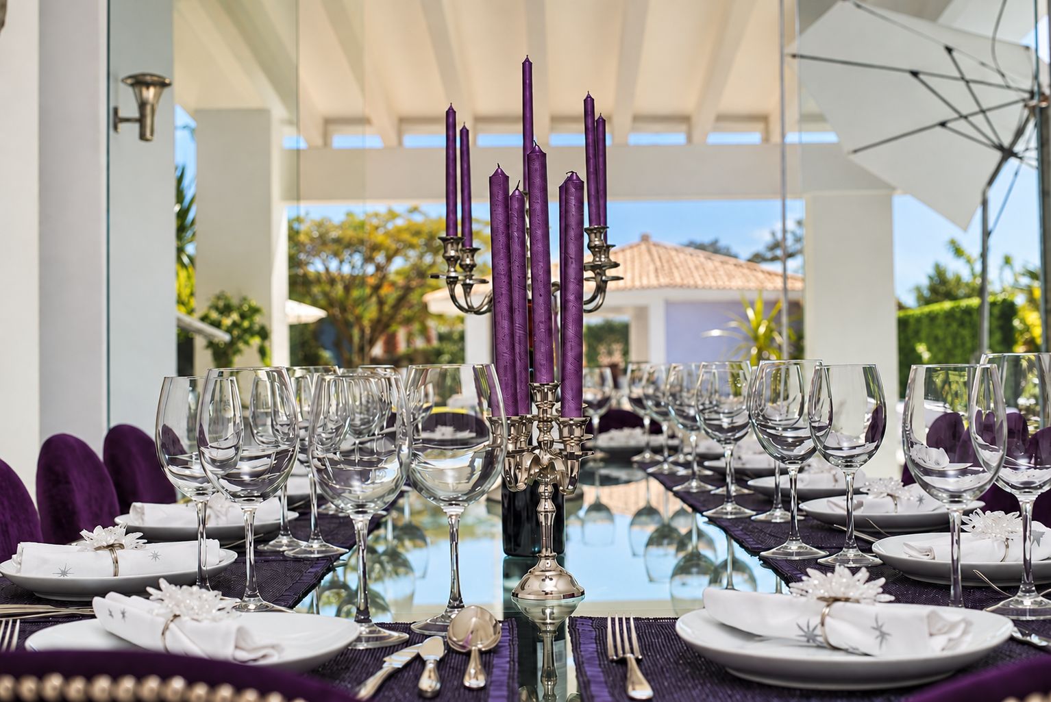 A table set for a formal dining experience with multiple wine glasses, plates, and a centerpiece of purple candles.