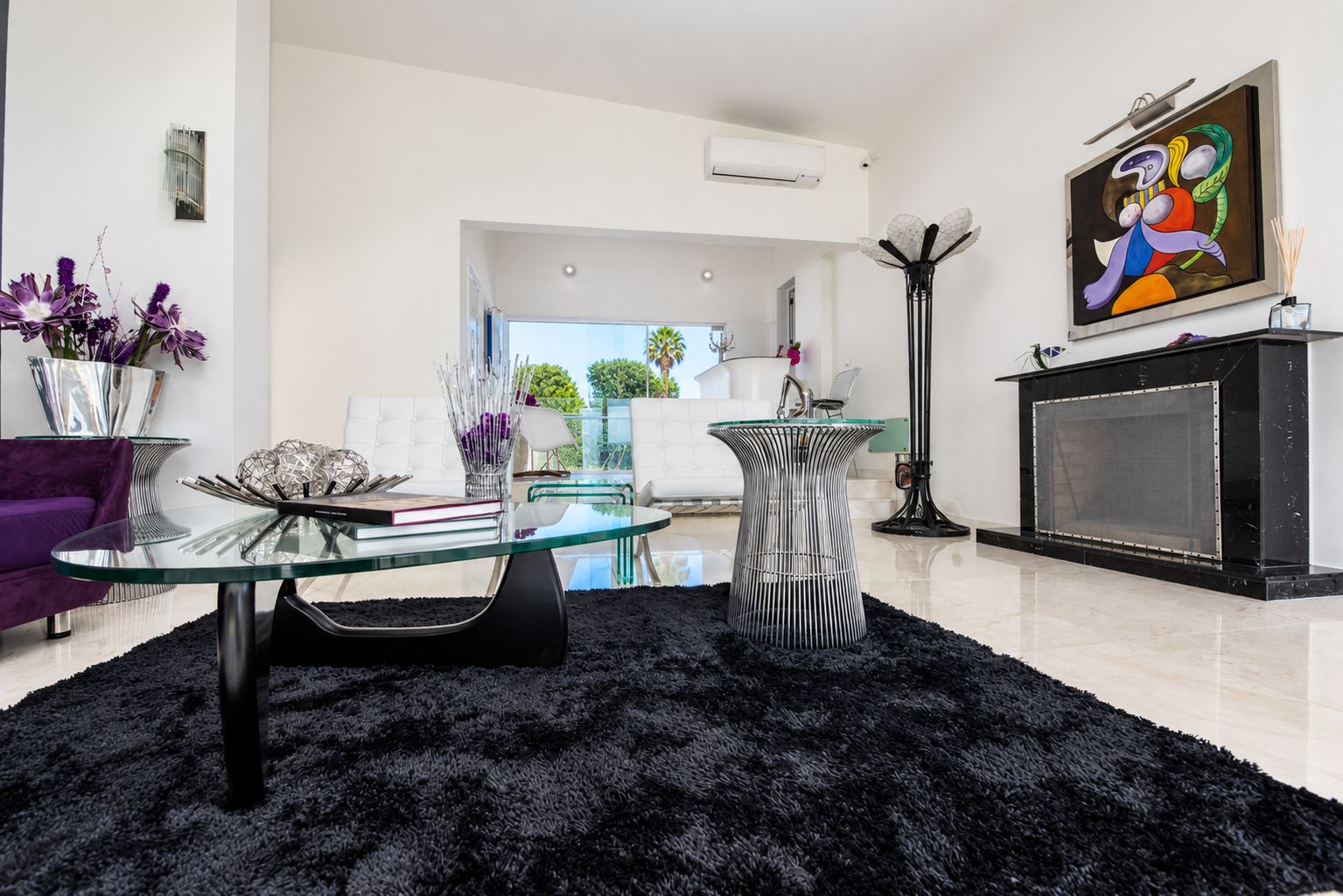 A modern living room with a glass coffee table, a black shag rug, a purple sofa, and a fireplace.
