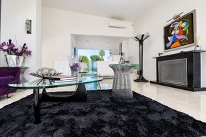 Una sala de estar moderna con una mesa de centro de vidrio, una alfombra peluda negra, un sofá púrpura y una chimenea.
