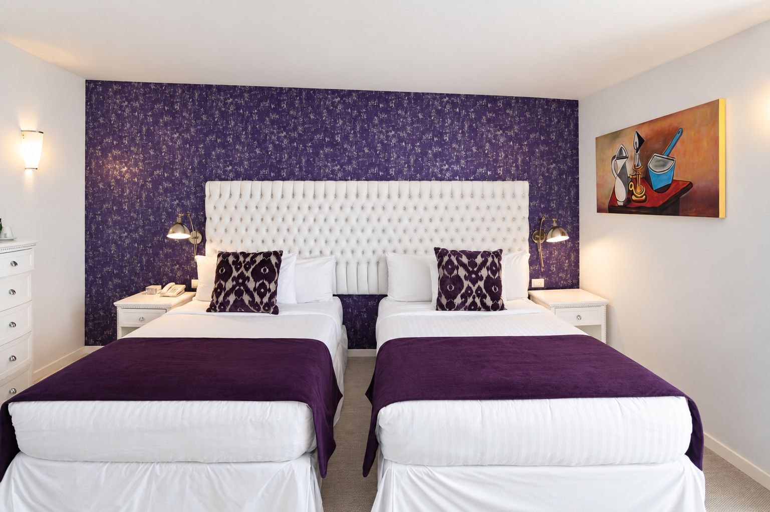 A double room with two beds, a headboard, bedside tables, lamps, a painting, and a dresser.