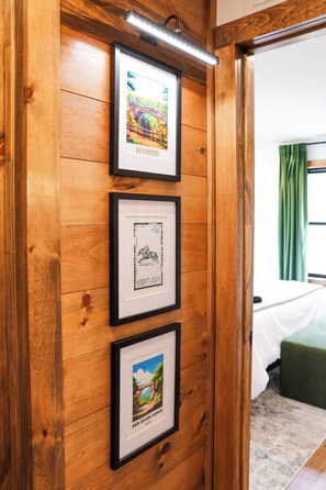 Un mur en bois orné de trois tableaux encadrés, un lit recouvert d’une couverture verte et une fenêtre avec des rideaux.