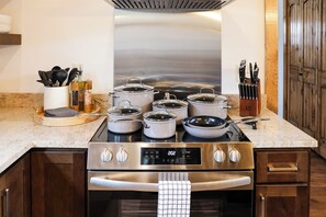 Een keuken met een roestvrijstalen fornuis en oven, diverse pannen, een messenblok en een kruidenrek.