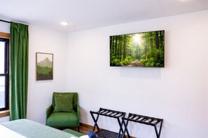 Une pièce comprenant un lit, un fauteuil vert, un banc, un tableau représentant une forêt et une fenêtre avec des rideaux verts.