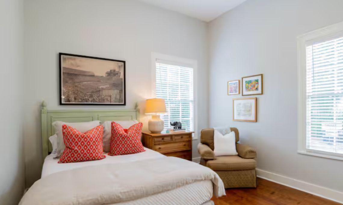 A bedroom with a bed, a nightstand, a chair, and a window with blinds.