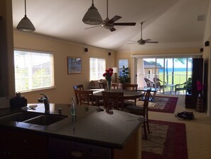 A kitchen with a central island, dining area with chairs, and a view of the outdoors. - Kai Lani – Beautiful Ocean View Condo In Paradise (Kapolei)