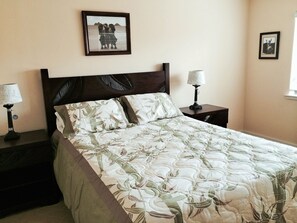 A bed with a floral bedspread, two bedside lamps, and a framed picture on the wall. - Kai Lani – Beautiful Ocean View Condo In Paradise (Kapolei)