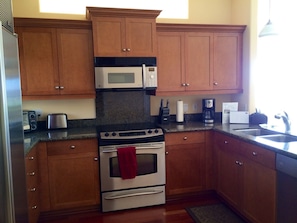 A kitchen with wooden cabinets, a stainless steel stove, a microwave, and a coffee maker. - Kai Lani – Beautiful Ocean View Condo In Paradise (Kapolei)