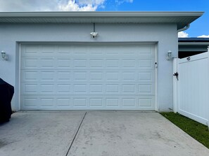 A garage with a white door, a concrete driveway, and a white fence. - The Disney Oasis - Your Disney Day! - Your Spa Night! (Kissimmee)