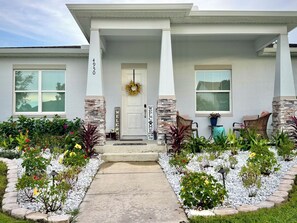 A residential house with a stone facade, a front door with a wreath, and a garden with various plants and a pathway. - The Disney Oasis - Your Disney Day! - Your Spa Night! (Kissimmee)